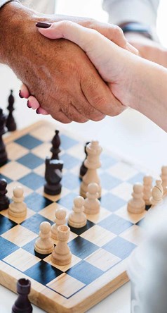 Two people shaking hands over a chess board